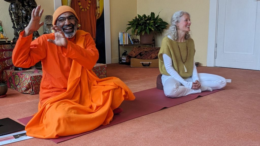 Links sitzt lachend und gestikulierend Swami Tattvarupananda aus Kerala. Rechts übersetzt Vishnuprema seine Allegorien.