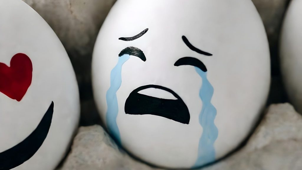 Mehrere mit Emojis bemalte Eier im Eierkarton. Im Vordergrund ein sehr sehr trauriges Ei.